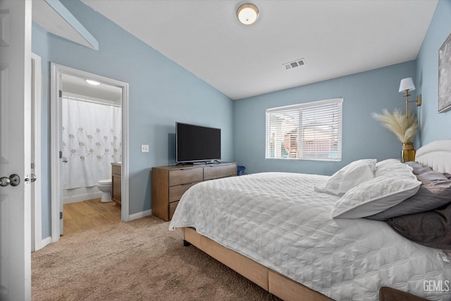 carpeted bedroom with ensuite bathroom and lofted ceiling