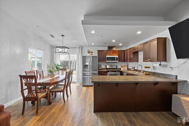 kitchen featuring pendant lighting, wood-type flooring, sink, kitchen peninsula, and stainless steel appliances