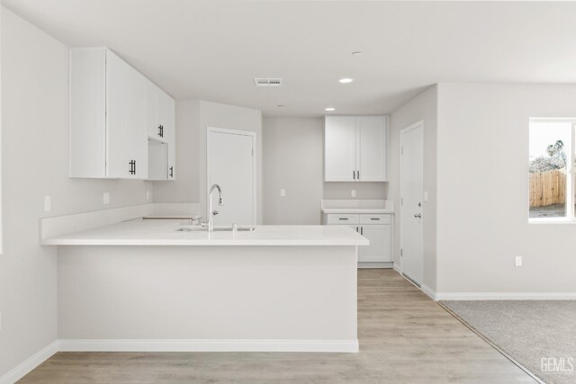 kitchen with a sink, light countertops, baseboards, and a peninsula