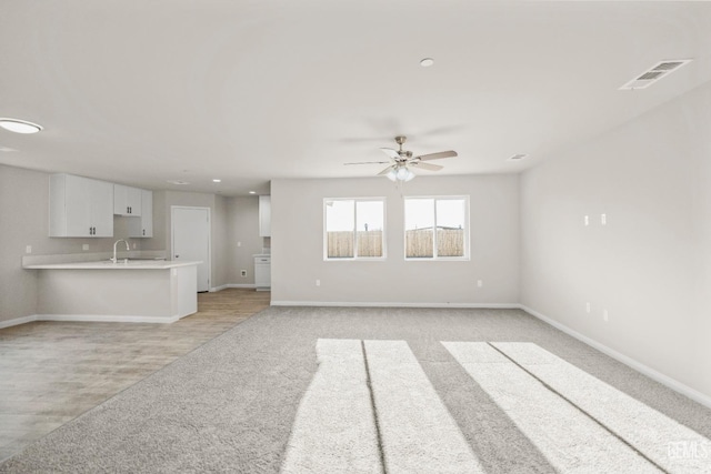 unfurnished living room featuring ceiling fan, visible vents, light colored carpet, a sink, and baseboards