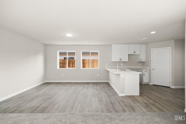 kitchen featuring baseboards, light countertops, white cabinets, a sink, and light wood-style flooring
