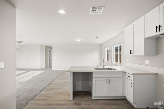 kitchen featuring visible vents, a peninsula, recessed lighting, white cabinetry, and a sink