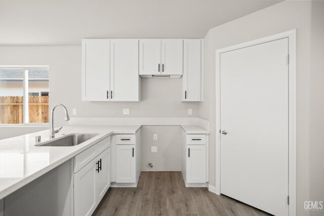 kitchen with white cabinets, light countertops, a sink, and wood finished floors