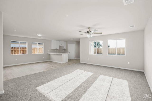 unfurnished living room with visible vents, a ceiling fan, a wealth of natural light, and light carpet