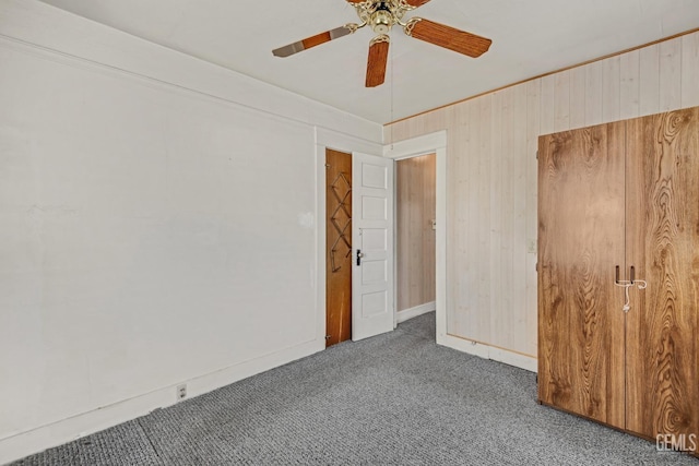 unfurnished bedroom with dark carpet, ceiling fan, and wood walls