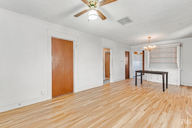 empty room with ceiling fan with notable chandelier, light hardwood / wood-style flooring, and a textured ceiling