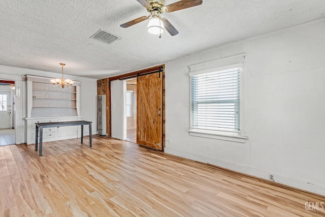 interior space with ceiling fan with notable chandelier, light hardwood / wood-style flooring, a barn door, and a textured ceiling