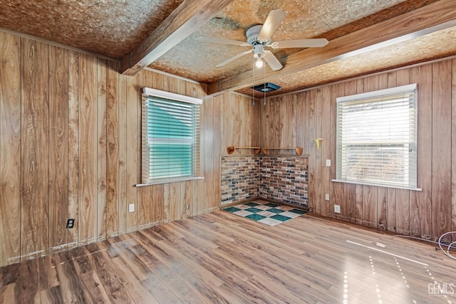 empty room featuring ceiling fan, wood-type flooring, and wood walls