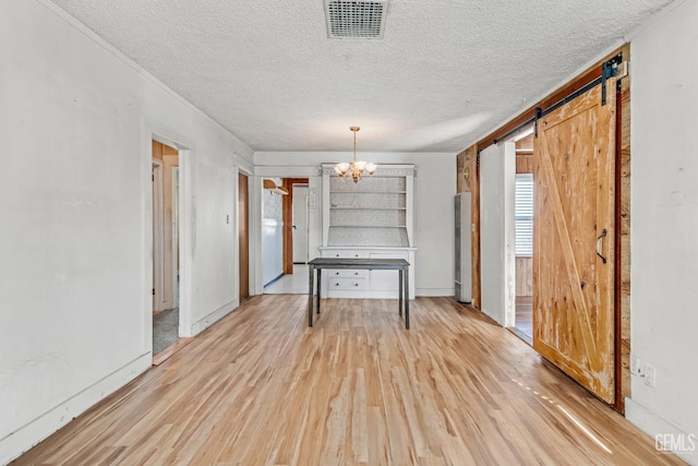 unfurnished dining area with a textured ceiling, a barn door, a chandelier, and light wood-type flooring