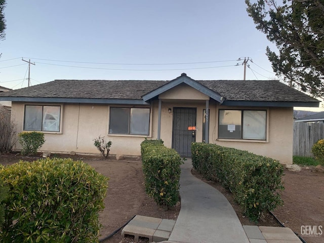 view of front of home with stucco siding, fence, and roof with shingles