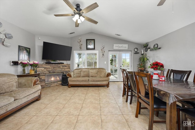 dining space with a ceiling fan, light tile patterned flooring, a fireplace, vaulted ceiling, and french doors