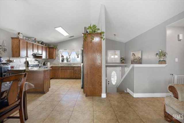 kitchen featuring a sink, stainless steel range, light countertops, under cabinet range hood, and brown cabinets