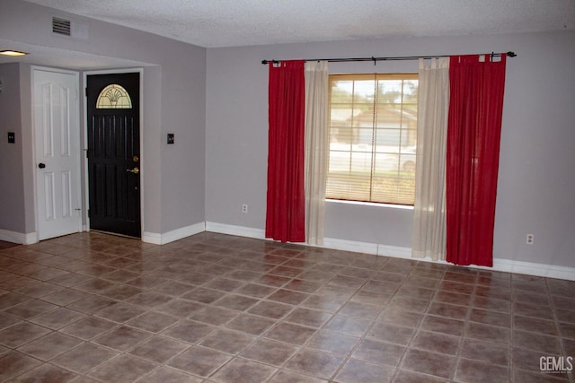 tiled entrance foyer with a textured ceiling, visible vents, and baseboards