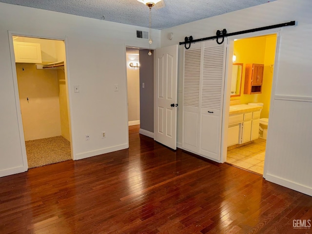 unfurnished bedroom featuring a barn door, visible vents, wood-type flooring, and a closet