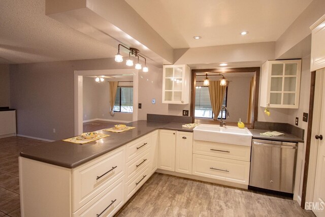 kitchen with stainless steel dishwasher, dark countertops, a sink, and white cabinets