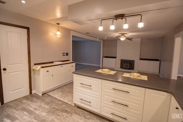 kitchen with dark countertops, ceiling fan, a wood stove, a peninsula, and white cabinetry