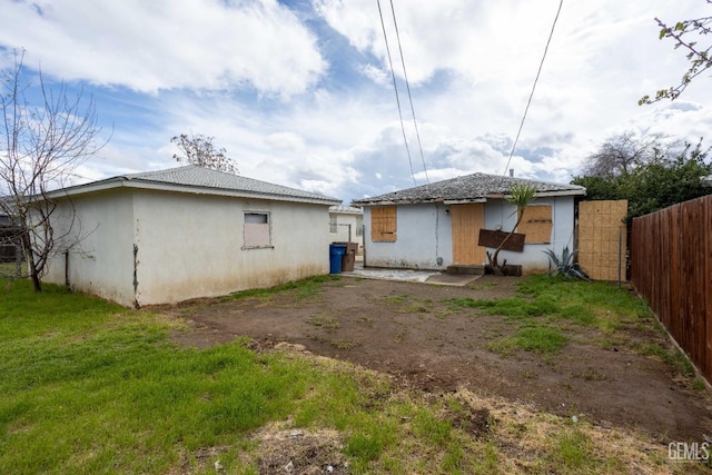 rear view of property with a yard, fence, and stucco siding