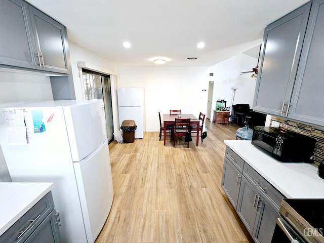 kitchen with backsplash, gray cabinets, white fridge, and light wood-type flooring