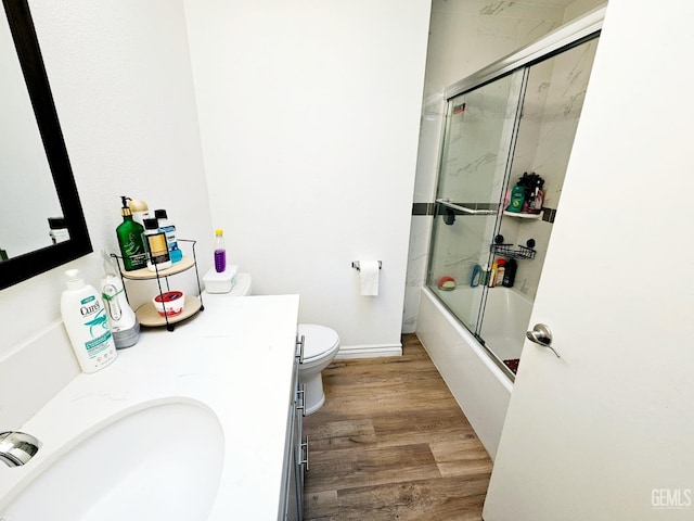 full bathroom with wood-type flooring, vanity, bath / shower combo with glass door, and toilet