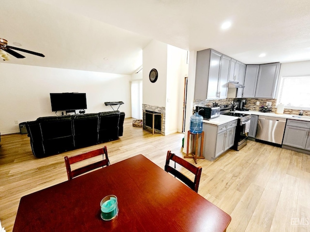 dining space featuring lofted ceiling, sink, ceiling fan, a fireplace, and light wood-type flooring