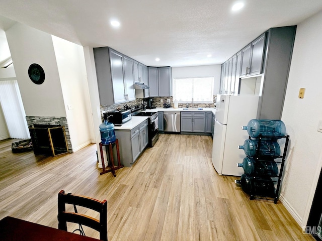 kitchen with appliances with stainless steel finishes, a fireplace, sink, gray cabinetry, and light hardwood / wood-style flooring