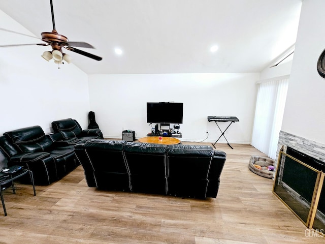 living room with ceiling fan, lofted ceiling, a stone fireplace, and light hardwood / wood-style flooring