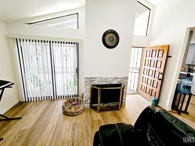 living room featuring high vaulted ceiling, a stone fireplace, and light hardwood / wood-style floors