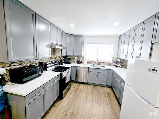 kitchen featuring gray cabinets, appliances with stainless steel finishes, sink, backsplash, and light wood-type flooring