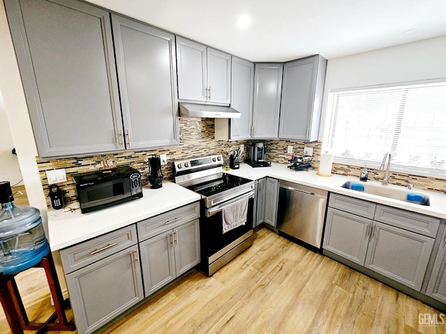 kitchen featuring sink, gray cabinetry, light hardwood / wood-style flooring, stainless steel appliances, and decorative backsplash