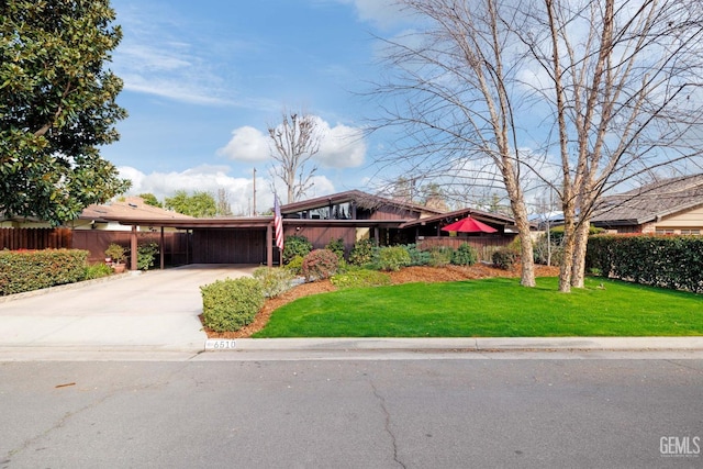 mid-century modern home featuring driveway, a front yard, and fence