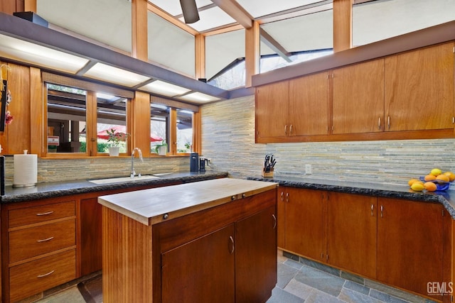 kitchen with a sink, decorative backsplash, a center island, stone finish floor, and dark countertops