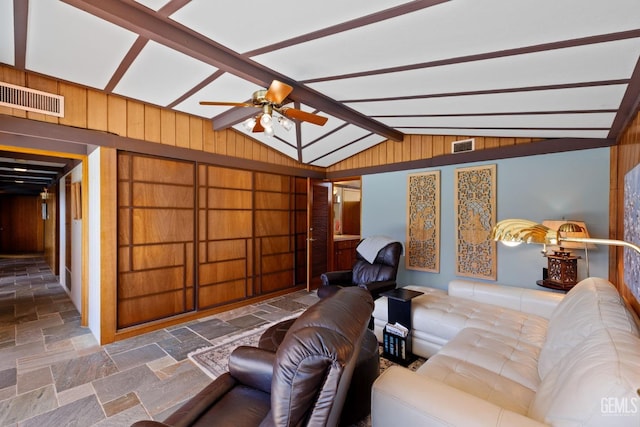 living area with vaulted ceiling with beams, stone tile floors, wooden walls, and visible vents