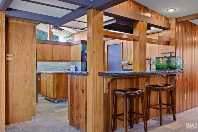 interior space featuring a dry bar, tasteful backsplash, stone finish flooring, wooden walls, and black refrigerator