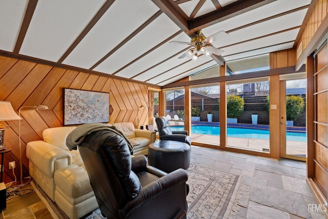 living area featuring lofted ceiling with beams, a wealth of natural light, wood walls, and stone tile flooring