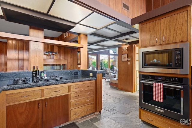 kitchen featuring black appliances, wooden walls, stone tile flooring, and brown cabinets