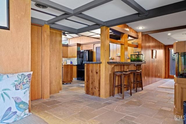 kitchen with a peninsula, beam ceiling, freestanding refrigerator, and stone tile floors