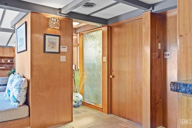 doorway featuring stone finish floor, beamed ceiling, and visible vents