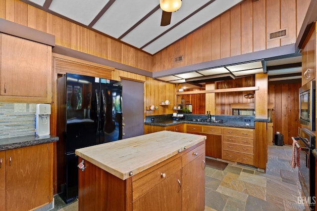 kitchen featuring wooden walls, stainless steel appliances, a kitchen island, vaulted ceiling, and stone finish floor