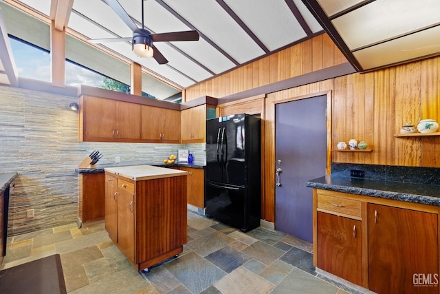 kitchen featuring freestanding refrigerator, a center island, stone finish floor, and dark countertops