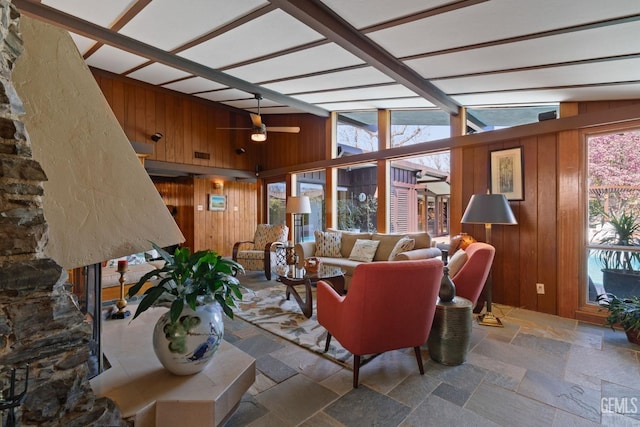 living area featuring wood walls, ceiling fan, and stone tile flooring