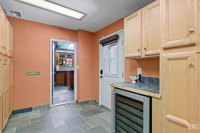 kitchen featuring wine cooler, dark countertops, stone tile flooring, visible vents, and light brown cabinetry