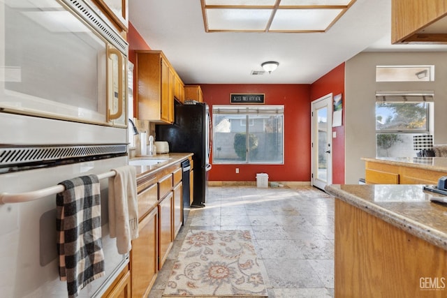 kitchen featuring oven, brown cabinetry, a sink, and stone tile flooring