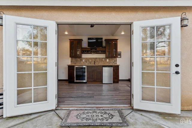 interior space with wine cooler, wood finished floors, dark brown cabinets, decorative backsplash, and glass insert cabinets