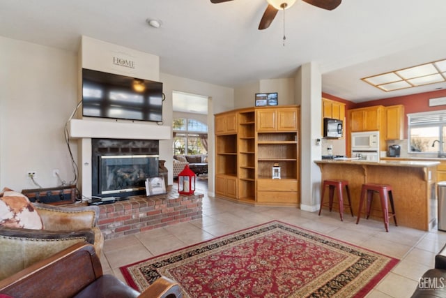 living room featuring light tile patterned floors, ceiling fan, and a brick fireplace