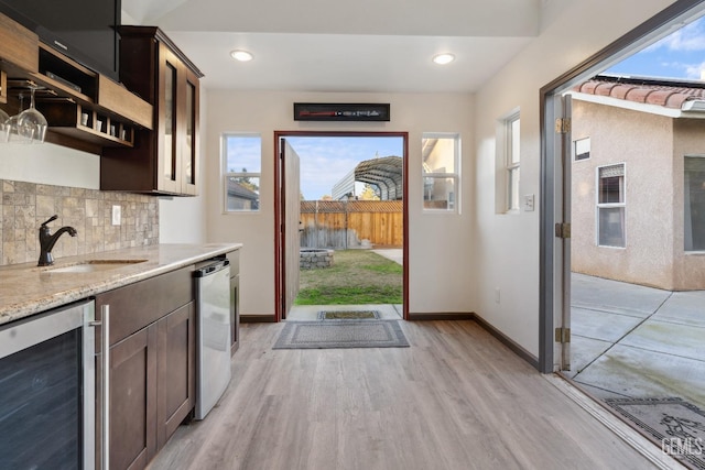 kitchen featuring light wood-style flooring, backsplash, a sink, dark brown cabinetry, and beverage cooler