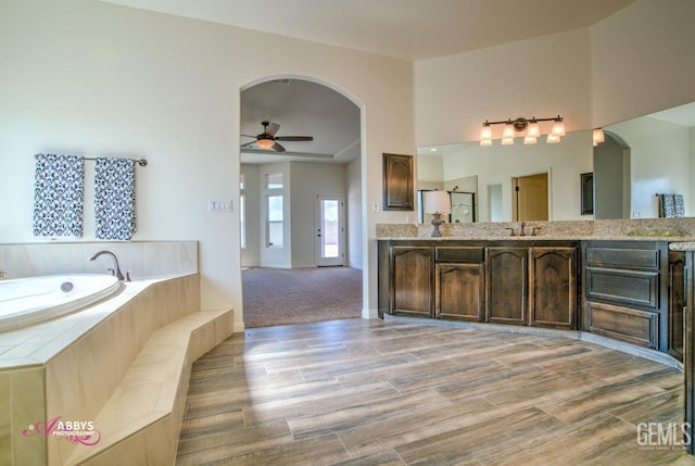 full bathroom featuring ceiling fan, wood finished floors, a garden tub, vanity, and baseboards