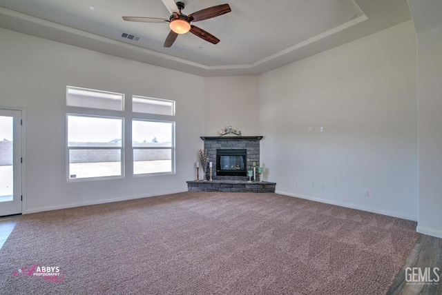 unfurnished living room with a tray ceiling, a ceiling fan, a fireplace, baseboards, and carpet flooring
