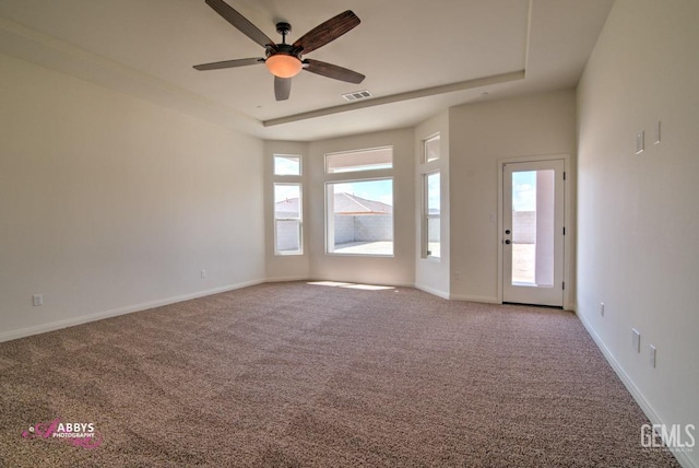 carpeted empty room featuring a raised ceiling, ceiling fan, and baseboards