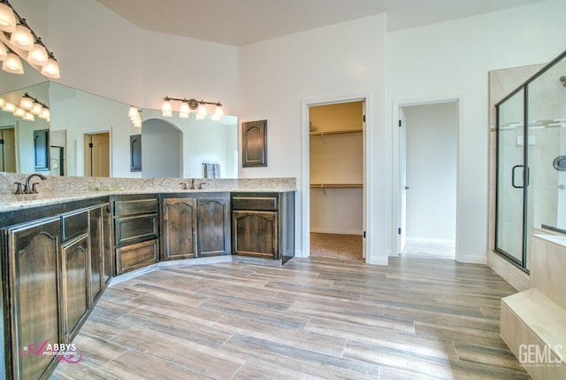 full bathroom with a shower stall, a spacious closet, double vanity, and wood finished floors
