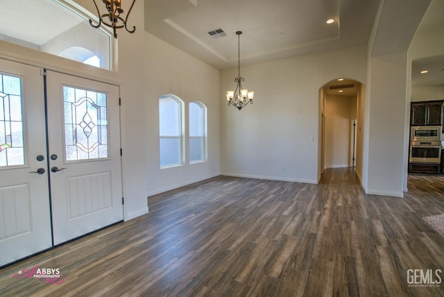 foyer with a chandelier, arched walkways, dark wood-style flooring, a raised ceiling, and healthy amount of natural light